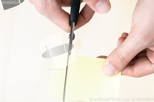 Image of A man is cutting a sheet of yellow paper using metallic scissors