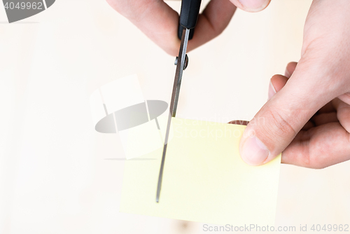 Image of A man is cutting a sheet of yellow paper using metallic scissors