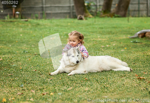 Image of The little baby girl playing with dog against green grass