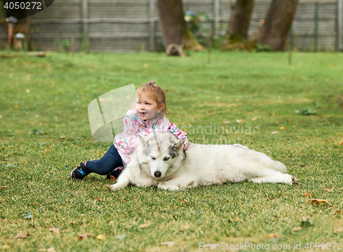 Image of The little baby girl playing with dog against green grass