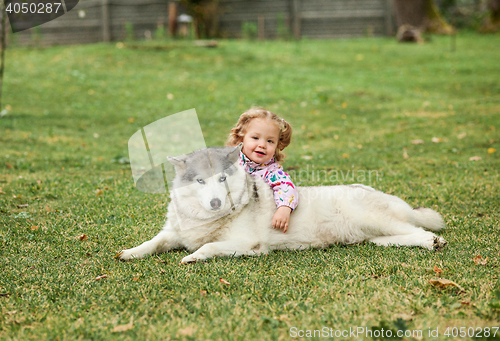 Image of The little baby girl playing with dog against green grass