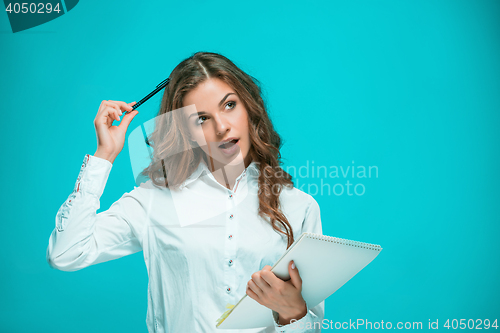 Image of The thoughtful young business woman with pen and tablet for notes on blue background