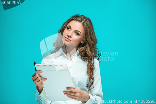 Image of The smiling young business woman with pen and tablet for notes on blue background