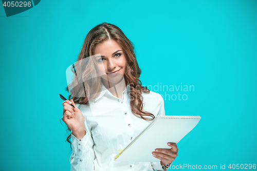 Image of The smiling young business woman with pen and tablet for notes on blue background