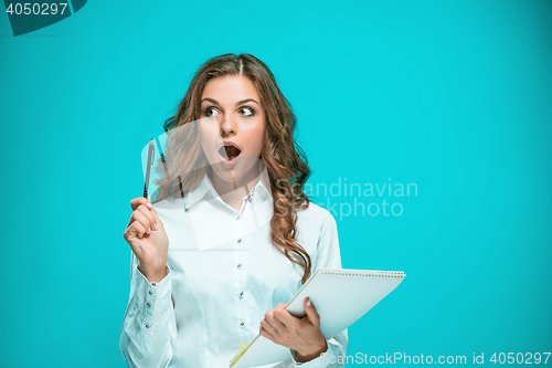 Image of Surprised young business woman with tablet for notes on blue background
