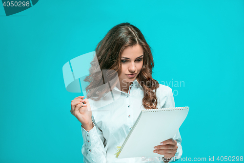 Image of The smiling young business woman with pen and tablet for notes on blue background