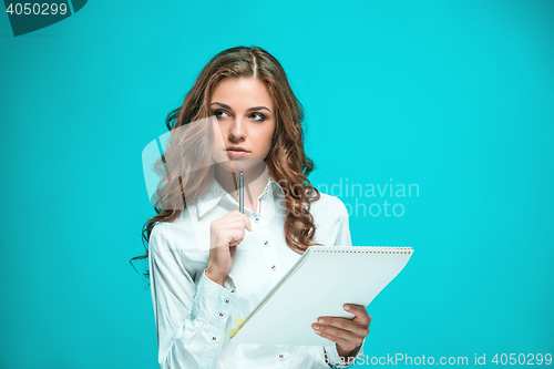 Image of The thoughtful young business woman with pen and tablet for notes on blue background