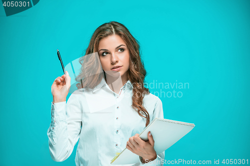 Image of The thoughtful young business woman with pen and tablet for notes on blue background