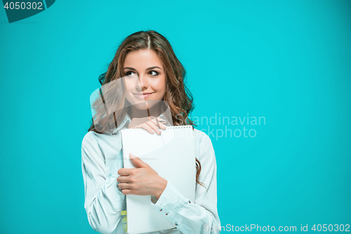 Image of The smiling young business woman with pen and tablet for notes on blue background