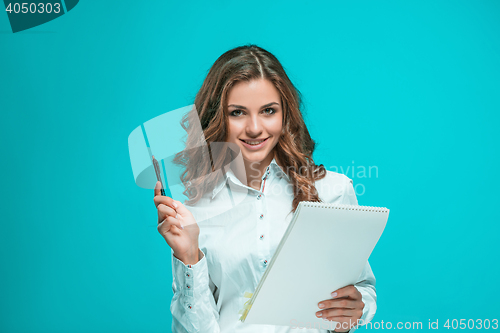 Image of The smiling young business woman with pen and tablet for notes on blue background