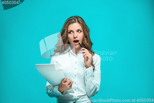 Image of The thoughtful young business woman with pen and tablet for notes on blue background