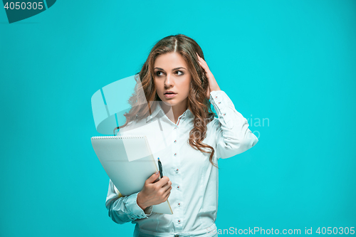 Image of The thoughtful young business woman with pen and tablet for notes on blue background