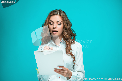 Image of The thoughtful young business woman with pen and tablet for notes on blue background