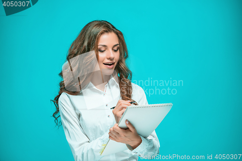 Image of The smiling young business woman with pen and tablet for notes on blue background