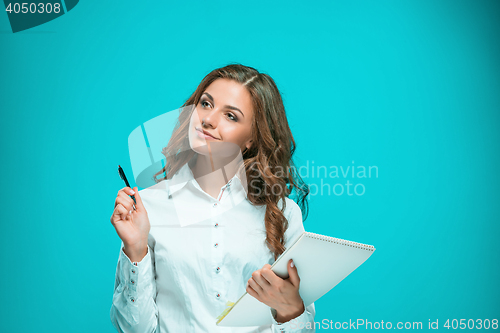 Image of The smiling young business woman with pen and tablet for notes on blue background