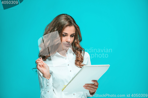 Image of The smiling young business woman with pen and tablet for notes on blue background