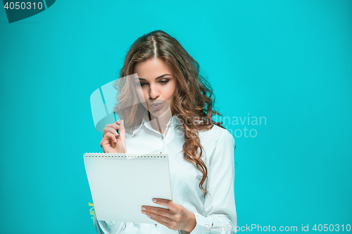 Image of The thoughtful young business woman with pen and tablet for notes on blue background