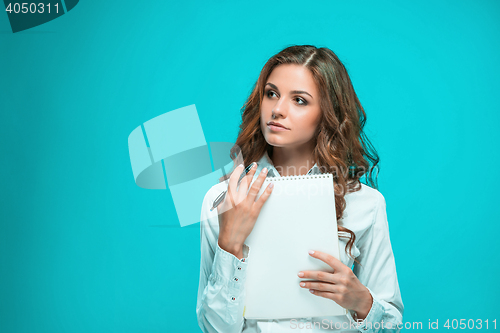 Image of The thoughtful young business woman with pen and tablet for notes on blue background