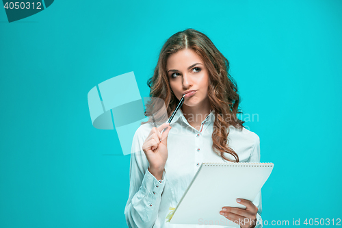Image of The thoughtful young business woman with pen and tablet for notes on blue background