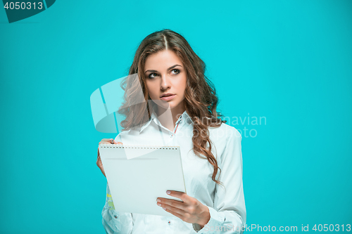 Image of The thoughtful young business woman with pen and tablet for notes on blue background