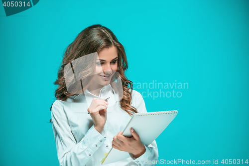 Image of The smiling young business woman with pen and tablet for notes on blue background