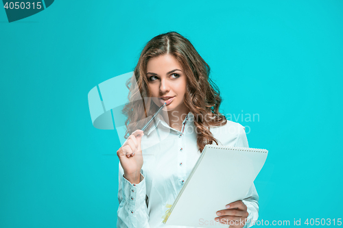 Image of The thoughtful young business woman with pen and tablet for notes on blue background