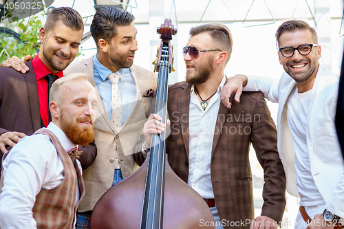 Image of Group of five stylish male friends talking and having fun outdoors, holding double bass