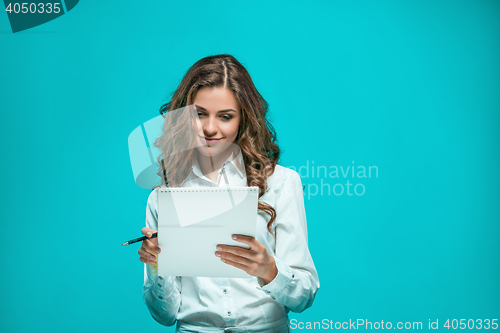 Image of The smiling young business woman with pen and tablet for notes on blue background