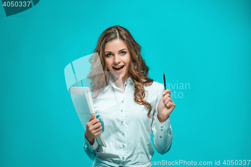 Image of The smiling young business woman with pen and tablet for notes on blue background