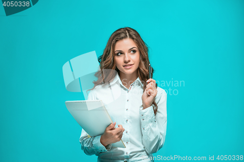 Image of The smiling young business woman with pen and tablet for notes on blue background