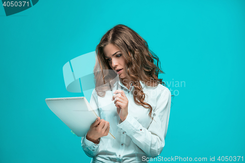 Image of The thoughtful young business woman with pen and tablet for notes on blue background