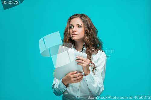 Image of The thoughtful young business woman with pen and tablet for notes on blue background