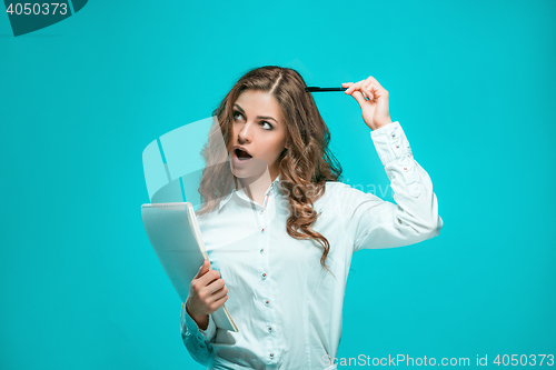 Image of The thoughtful young business woman with pen and tablet for notes on blue background