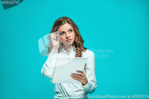 Image of The thoughtful young business woman with pen and tablet for notes on blue background