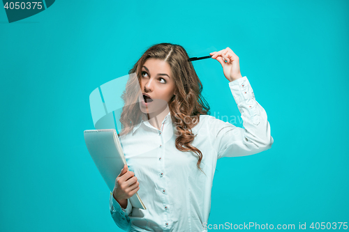 Image of The thoughtful young business woman with pen and tablet for notes on blue background