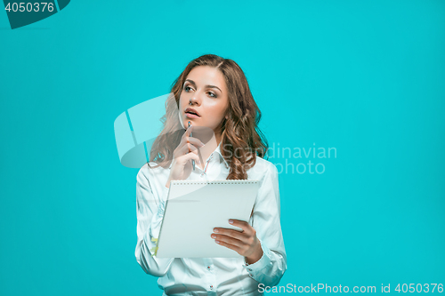 Image of The thoughtful young business woman with pen and tablet for notes on blue background