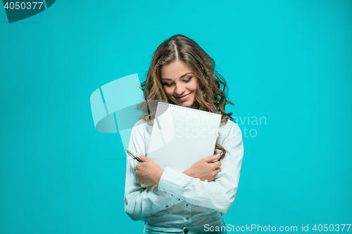 Image of The smiling young business woman with pen and tablet for notes on blue background