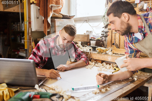 Image of carpenters with laptop and blueprint at workshop