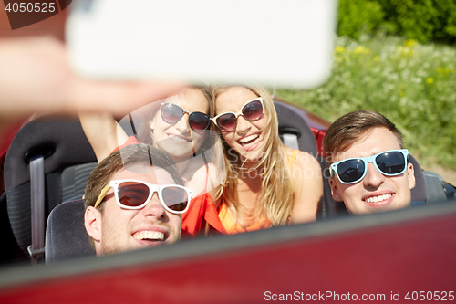 Image of friends driving in cabriolet car and taking selfie