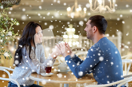 Image of happy couple with tea holding hands at restaurant