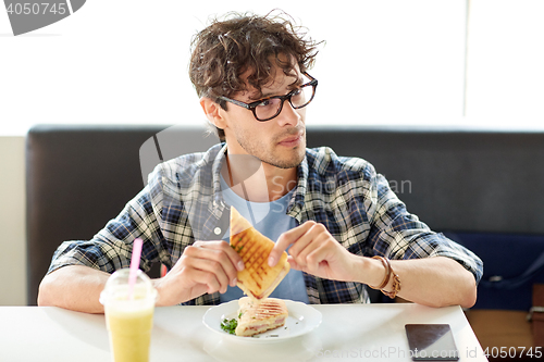 Image of happy man eating sandwich at cafe for lunch