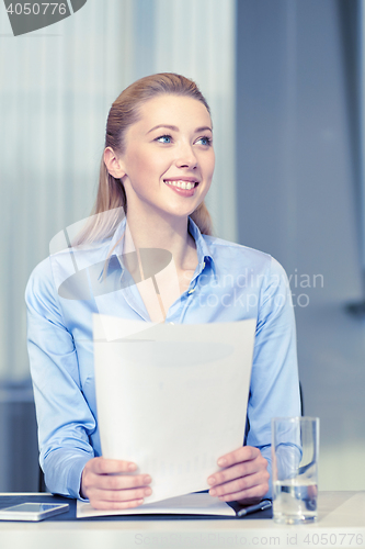 Image of smiling woman holding papers in office