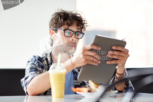 Image of man with tablet pc and earphones sitting at cafe