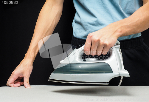 Image of Male person using a steaming hot iron, on a iron board on black