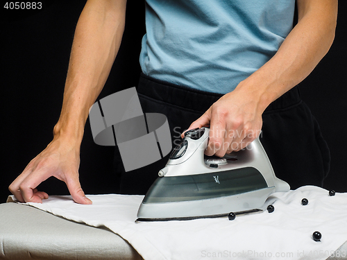 Image of Male person using a steaming hot iron, on a white shirt