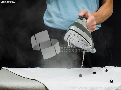 Image of Male person using a steaming hot iron, on a white shirt