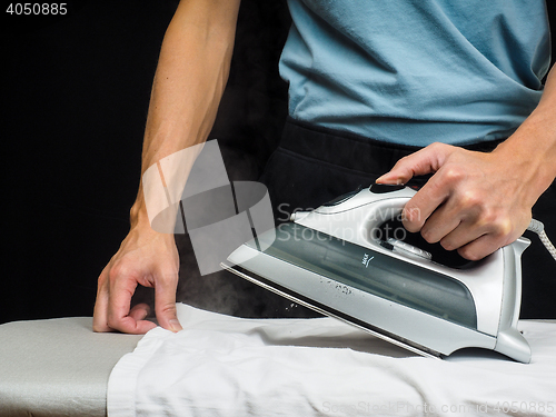 Image of Male person using a steaming hot iron, on a white shirt