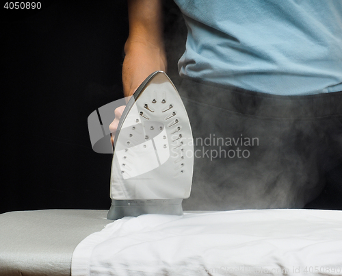 Image of Male person using a steaming hot iron on a white shirt