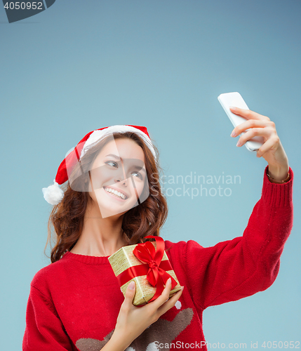 Image of Girl dressed in santa hat with a Christmas gift and phone