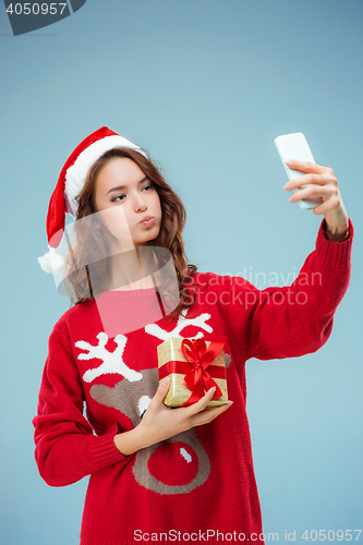 Image of Girl dressed in santa hat with a Christmas gift and phone